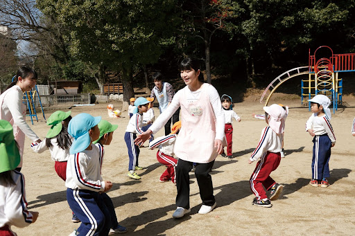 園庭で遊ぶたくさんの子供たちと先生