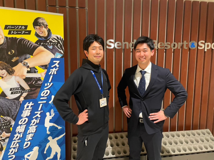 仙台リゾート＆スポーツ専門学校の前でポーズをとる2人の男性