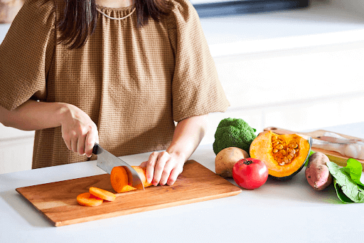 ニンジンを切る女性と多くの野菜